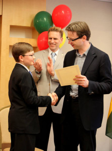 Lietuvos ambasadorius JAV Rolandas Kriščiūnas įteikia Augustui mokyklos baigimo pažymėjimą, kuriuo džiaugiasi ir istorijos mokytojas Audrius Kirvelaitis. 